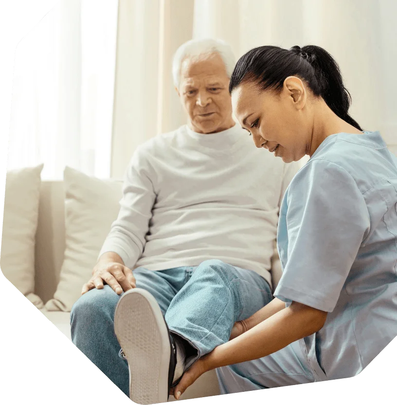 This image appears to show a healthcare professional performing a physical assessment or rehabilitation session on an older adult in a home setting